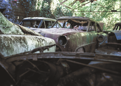 Photographie urbex de plusieurs vieilles voitures abandonnées sous un hangar dans une forêt par le rat graphiste.